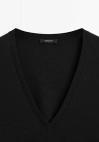Schwarzes V-Ausschnitt-T-Shirt mit glatter Textur, das ein sauberes Design aufweist und ein Etikett mit "Massimo Dutti, Made in China" am Ausschnitt hat.