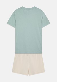 Camiseta de algodón azul claro con mangas cortas y cuello redondo, combinada con pantalones cortos color crema hechos de una tela suave. Diseño sencillo, sin patrones.
