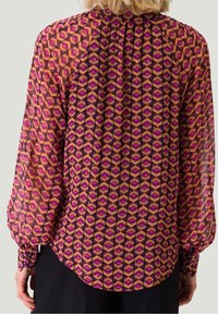 Gennemsigtig bluse i en livlig pink og lilla geometrisk mønster, med lange ærmer, samling ved halsen og en buet kant. Blødt, letvægtsstof.
