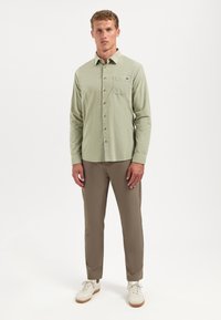 Lichtgroen katoenen shirt met een button-down kraag, borstzak en lange mouwen, gecombineerd met tan kleurige broek en witte sneakers.