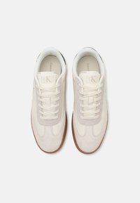 Zapatillas Calvin Klein en ante de color blanco roto y beige, con cierre de cordones, forro textil suave y suela de goma con un patrón texturizado.