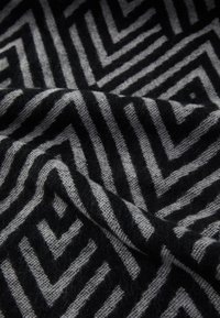 Tissu à motifs noir et gris présentant un design géométrique en zigzag, avec une texture douce et un aspect tissé.