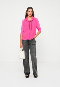Felle roze coltrui met zwarte trekkoord, gecombineerd met hoog-waisted zwarte denim jeans. Gemaakt af met een kleine witte handtas.