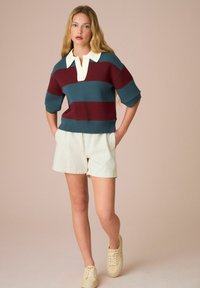 Sweter dzianinowy w kolorze morskim, w burgundowe paski, z jasnobeżowym kołnierzykiem. Połączony z jasnobeżowymi krótkimi spodniami w paski i beżowymi trampkami.