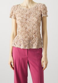Lososové květinové krajkové tričko s krátkými rukávy a siluetou peplum, doplněné růžovými kalhotami na míru, které ukazují složité květinové vzory.