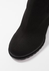 Botín negro con parte superior de punto texturizado, puntera redonda y suela de goma. Sin herrajes visibles, enfatiza un diseño suave.