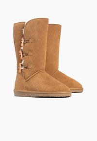 Stivali al ginocchio in suede tan con tre bottoni a toggle in legno e una texture morbida. Punta arrotondata e suola in gomma piatta progettata per il comfort.