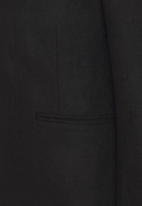 Černý vlněný kabát s hladkou texturou, upraveným střihem a jedním šikmým kapsou na levé straně. Jednoduchý a elegantní design.