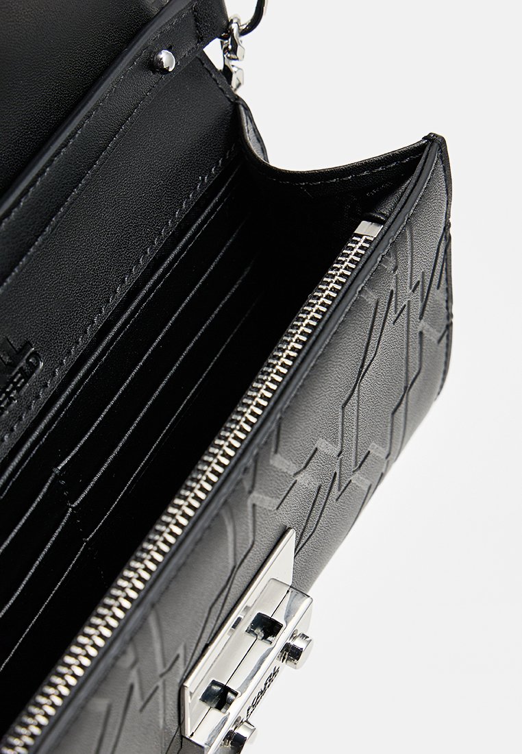 Sac à main en cuir noir avec un motif en zigzag texturé, fermeture à glissière en argent, plusieurs emplacements pour cartes à l'intérieur et un accent en métal argenté brillant.