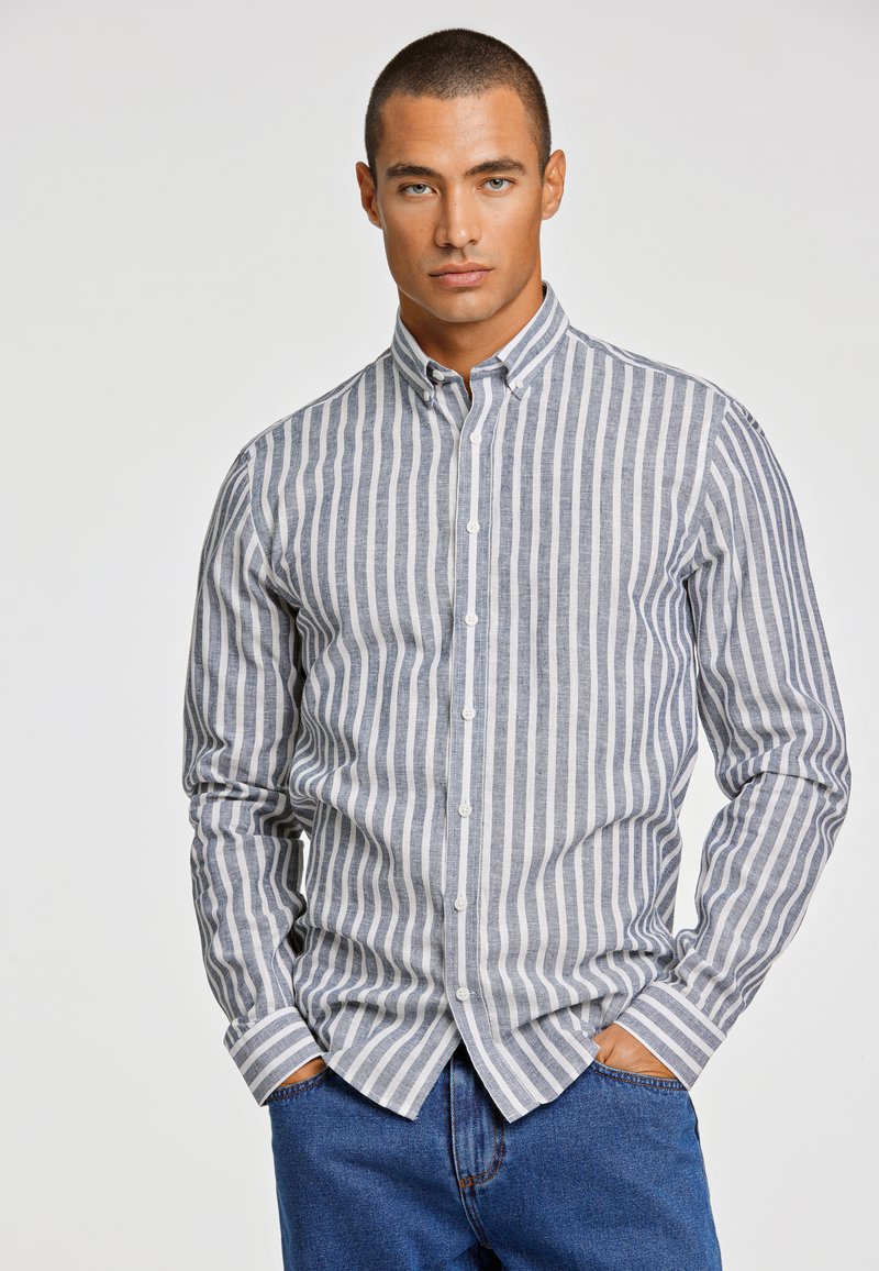 Camicia a righe con bottoni in grigio chiaro e blu navy, caratterizzata da maniche lunghe, colletto e bottoni frontali. Tessuto testurizzato con righe verticali.