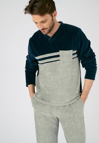 Conjunto de loungewear suave en gris y azul marino con escote en V, diseño de rayas horizontales y un bolsillo frontal. Los pantalones tienen bolsillos laterales.