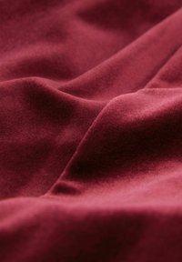 Burgunderfarbener Stoff mit einer weichen, samtigen Textur, der sanfte Drapierungen und einen subtilen Glanz aufweist, der die reiche Farbe und die luxuriöse Oberfläche hervorhebt.