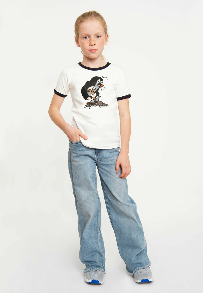 White t-shirt with black trim featuring a cartoon mole graphic, paired with light blue wide-leg jeans and gray sneakers. Smooth fabric texture.