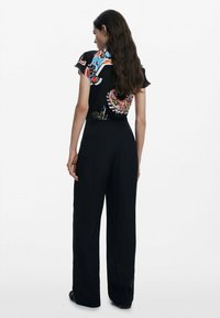 Black wide-leg jumpsuit with short sleeves features a colorful floral design on the back, smooth fabric, and a fitted waist.