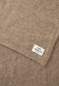 Beige knit scarf made of soft fabric, featuring a subtle texture and a white brand label with "MADS NØRGAARD COPENHAGEN" printed on it.