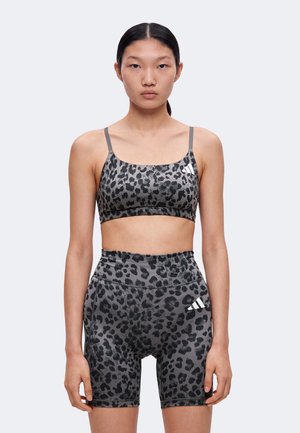 Young kvinde med glat sort hår bærer grå og sort leopardprint sports-bh og matchende høj-taljede biker-shorts med hvidt logo.