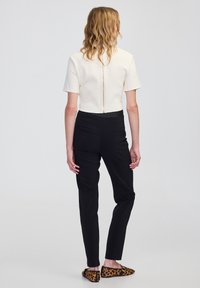 Crème top met korte mouwen en een hoge kraag, gecombineerd met zwarte, op maat gemaakte broeken en instappers met luipaardprint.