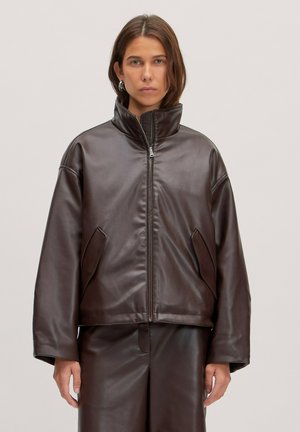 Bruine nepleren jas met hoge kraag, ritssluiting en zijzakken. Oversized pasvorm met een gladde textuur en minimalistisch ontwerp.