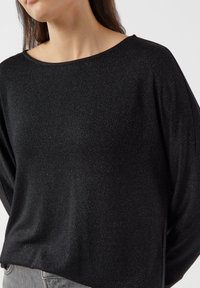 Czarna bluzka o luźnym kroju, z szerokim dekoltem typu łódka i długimi rękawami. Materiał ma subtelny, błyszczący połysk, który podkreśla jej atrakcyjny wygląd.