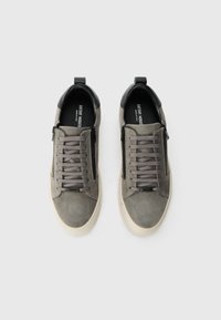 Et par grå ruskinds lace-up sneakers med sidelommer og sorte accenter, set ovenfra på en hvid baggrund.