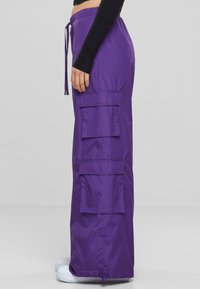 Lila Cargo-Hosen mit einem Kordelzugbund, die über mehrere Seitentaschen und ein gerades Bein-Design verfügen. Hergestellt aus einem glatten, leichten Material.