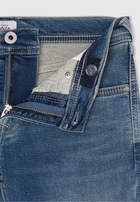 Farkkuhaalari, jossa on vetoketjukiinnitys, nappikiinnitys ja vaaleansinen pesu, jossa on kuvioitu sisävuori ja standardi viiden taskun design.