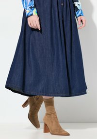 Jupe en denim avec une forme évasée et une teinte bleu foncé, associée à des bottines en suede marron clair avec un talon carré.