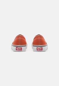 Scarpe slip-on rosse in tela con suole in gomma bianche, caratterizzate da cuciture a contrasto e da un'etichetta con logo sul tallone.