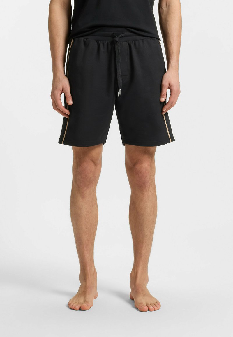 Zwarte katoenen shorts met een elastische tailleband en trekkoord. Kenmerkt zijsstrips in een lichtere kleur. Tot slot, knielange stijl.