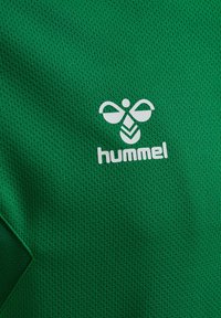 Grøn sports T-shirt med en struktureret stof. Har et hvidt logo af en stiliseret bi og mærkenavnet "hummel" nedenfor logoet.
