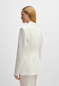 White tailored blazer with structured shoulders, smooth texture, and a subtle seam detail at the back. Minimalist design without embellishments.