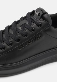 Sorte lædersneakers med tekstureret overdel, flade sorte snørebånd og prægede logo. Har en glat gummisål og subtile syninger.