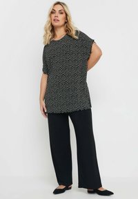 Top a pois bianco e nero con vestibilità rilassata, maniche corte e orlo arrotondato, abbinato a pantaloni neri a gamba larga e scarpe nere flat.