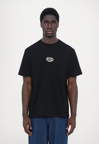 Camiseta de algodón negra con cuello redondo, que presenta un logo ovalado blanco central que dice "<ARROW>". Tiene mangas cortas y un diseño de corte relajado.