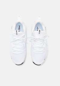 White athletic shoes with mesh upper, flat laces, and a pull tab. Black outsole and 'Nike Free' branding on tongue. Minimal design.