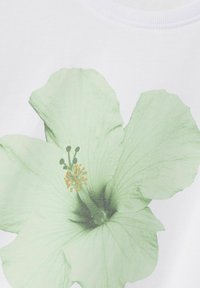 Balta krekla ar lielu, gaiši zaļu hibiska zieda motīvu ar tumšāku ēnojumu un dzeltenu putekšņu detaļu. Gluda tekstūra, apaļa kakla izgriezuma forma.