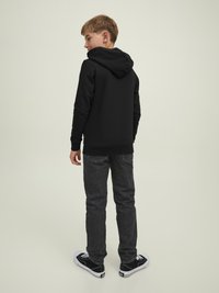 Felpa nera con cappuccio, jeans grigi e sneakers nere. L'outfit presenta un design semplice, senza logo, e una vestibilità comoda.