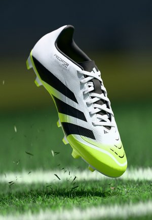 White and black cleat with lime green accents, featuring a textured upper, six studs, and the word "Predator" on the side.