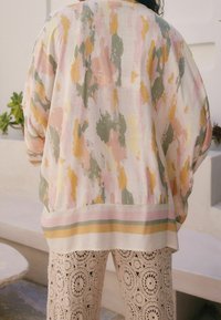 Lightweight, pastel-hued top features a textured, abstract pattern with green, pink, and yellow accents. Below, intricate lace-like trousers.