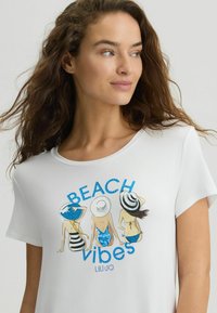 Biała koszulka z krótkim rękawem z kolorowym nadrukiem trzech postaci w kapeluszach plażowych i kostiumach kąpielowych, z napisem "BEACH VIBES."