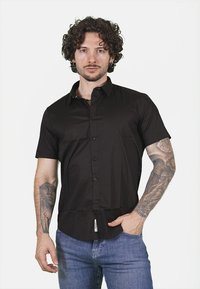 Camicia nera a maniche corte con bottoni, dal tessuto liscio e dalla vestibilità rilassata, abbinata a jeans blu aderenti.