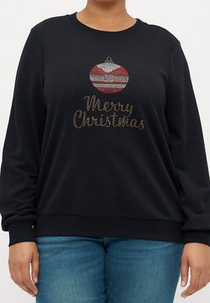 Sort langærmet sweater med rød og hvid ornamentdetalje og teksten "Glædelig Jul" i guldnitter foran, båret med blå jeans.