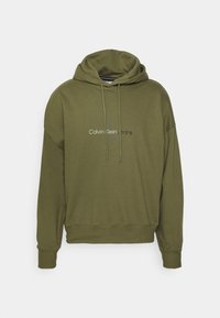 Olivengrønn hettegenser laget av myk stoff, med frontlomme, ribbestrikkede mansjetter, og hvitt "Calvin Klein Jeans"-logo.