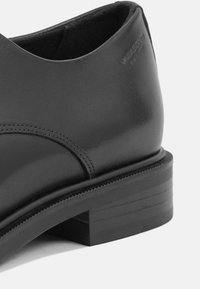 Black leather dress shoe with a rounded toe, subtle stitching, and a rectangular block heel featuring textured accents.