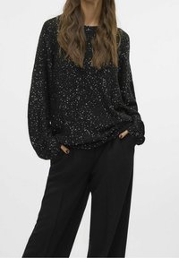 Zwarte trui met een gestructureerde afwerking, voorzien van zilveren pailletten verspreid over het geheel, gecombineerd met zwarte wijde broekspijpen.