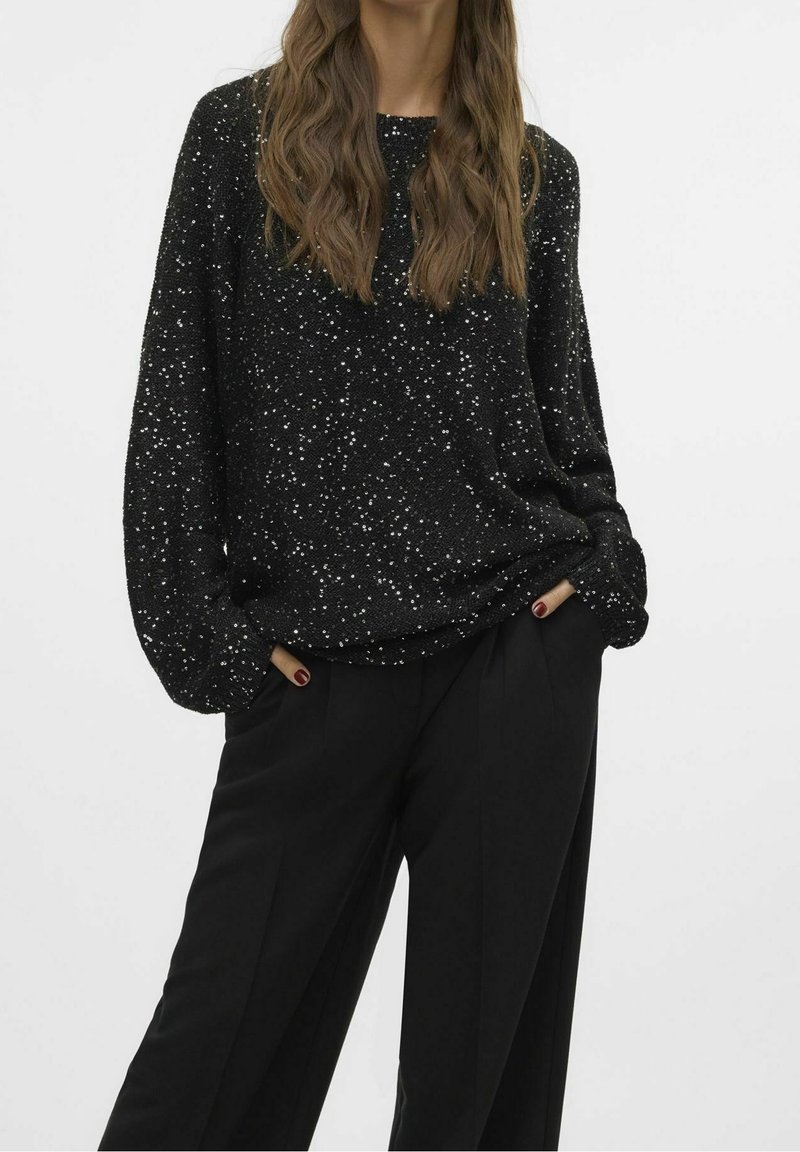 Zwarte trui met een gestructureerde afwerking, voorzien van zilveren pailletten verspreid over het geheel, gecombineerd met zwarte wijde broekspijpen.
