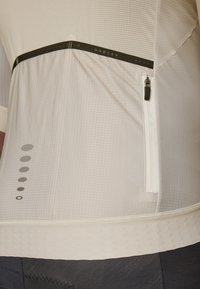 Weißes Sportshirt aus strukturiertem Stoff, mit einer schwarzen Akzent-Reißverschlusstasche und kleinen Designelementen in Grau entlang der Seite.