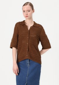 Brun strikket cardigan med kragehals, korte ermer og hule mønstre. Har frontknapper og en avslappet passform.