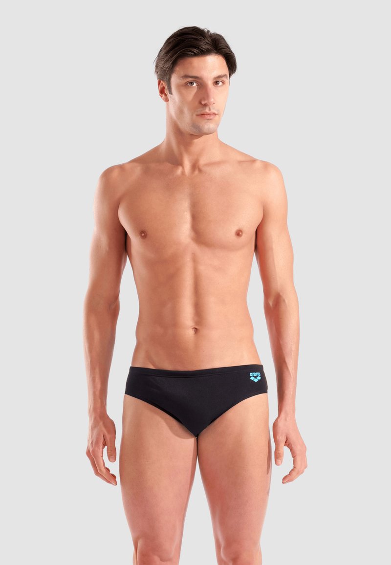 Costume da bagno nero in tessuto morbido, con un sottile logo blu sulla vita. Design minimalista con vestibilità aderente.