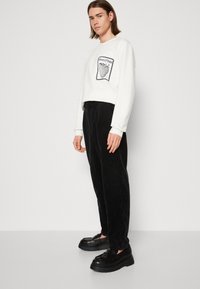 Hanorac alb scurt cu un design în formă de inimă neagră. Asortat cu pantaloni negri din catifea ripsată și pantofi masivi negri. Texturi netede, croială lejeră.